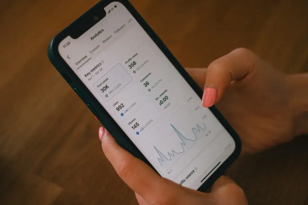 Hands holding a smartphone showing a social analytics overview with key metrics and a trend graph
